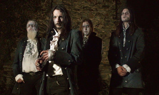 Bandfoto van Crux Tenebris: vier muzikanten in donkere historische kostuums en corpsepaint voor een stenen muur