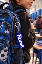 Acusinkt gepersonaliseerde naam-sleutelhanger in blauw aan een blauwe schooltas