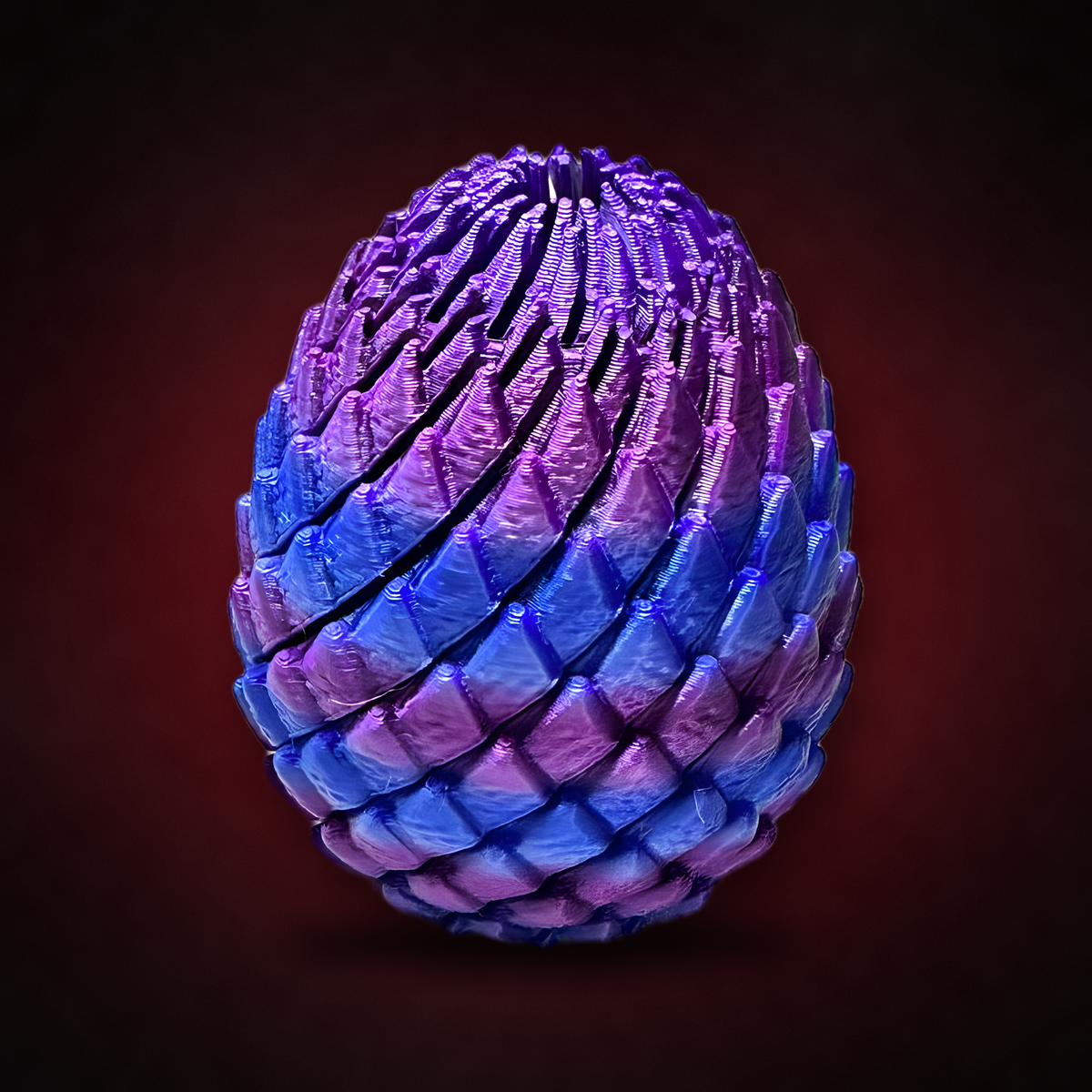 Acusinkt œuf de dragon (Drakenei) irisé violet-bleu-rose, fidget sur fond sombre avec une lueur rouge vin.