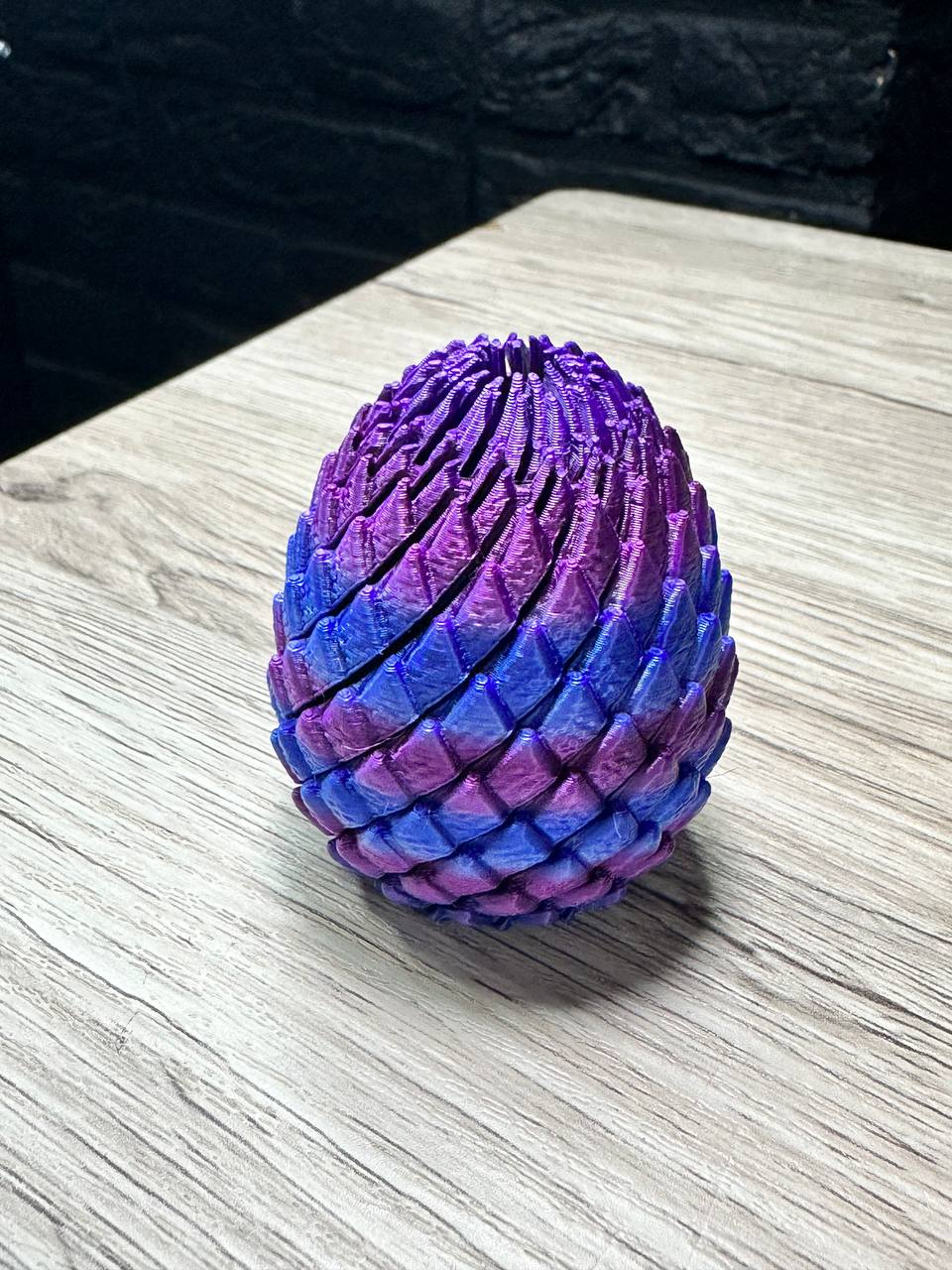 Acusinkt Drakenei in iriserend paars-blauw-roze, gesloten ei op tafel met rijen schubben.