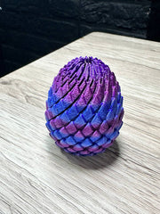 Acusinkt Drakenei in iriserend paars-blauw-roze, gesloten ei op tafel met rijen schubben.