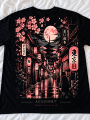 Detail van de achterkant van het zwarte Sakura Street T-shirt op een wit laken: sakura-takken, volle maan, pagode, gloeiende lantaarns en een kat in roze en crème tinten